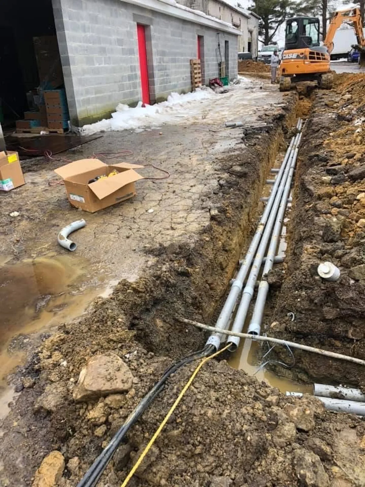 Commercial underground conduit trench with excavator on site